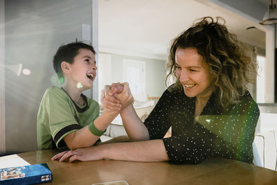 Playful mother arm wrestling with son on table at home