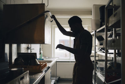 Silhouette of male baker washing dishes while working in commercial kitchen