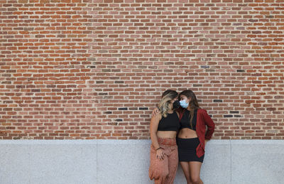 Two young girls with mask standing against brick wall