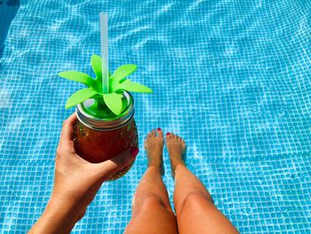 Low section of woman with drink in swimming pool