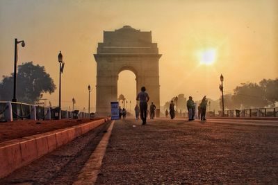 People on road against gate during sunset