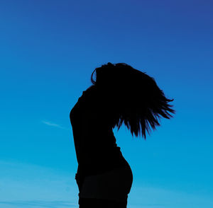 Low angle view of silhouette woman standing against blue sky