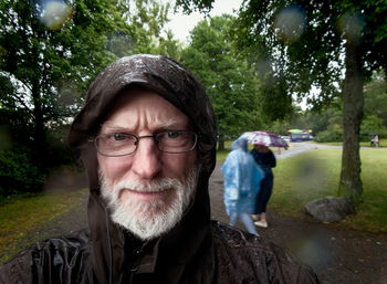 Portrait of senior man wearing raincoat at park during rainy season
