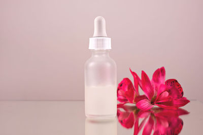 Face serum oil drop with dropper glass bottle pipette pink flowers background close up