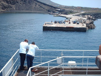 Rear view of friends standing on railing against sea