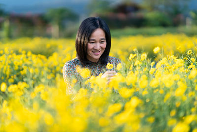 Portrait of smiling young woman with yellow flowers on field