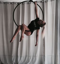 Woman performing acrobat on ring against curtain