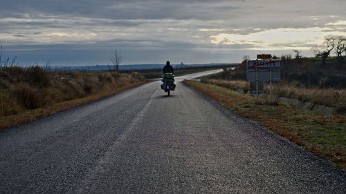 Rear view of man riding bicycle on road against sky