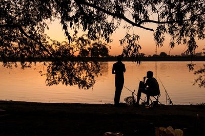 Silhouette people at lakeshore against sky during sunset