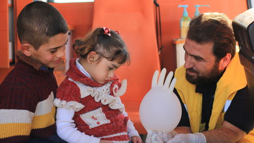 Doctor with glove balloon talking to daughter at home