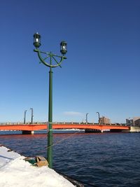 Street light by sea against clear blue sky