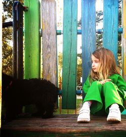 Cute girl sitting against fence at park