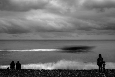 Rear view of people looking at sea against cloudy sky