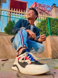 Teenage boy in sunglasses crouching against building