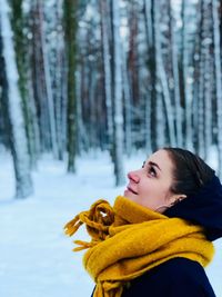 Profile view of thoughtful young woman standing against trees in forest during winter