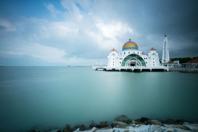 View of building by sea against cloudy sky