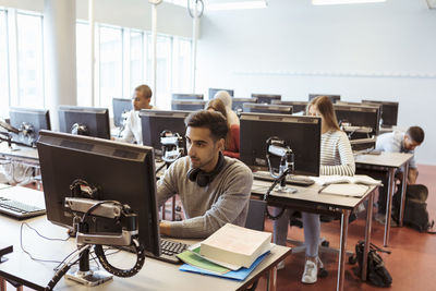 Male and female students using computers at library in university