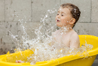 Cute little boy bathing in yellow tub outdoors. happy child is splashing, playing with water