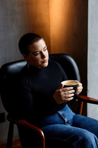 Young woman holding coffee cup while sitting on chair