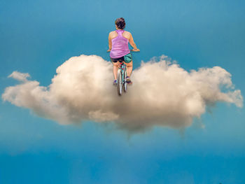 Low angle view of man riding bicycle against blue sky