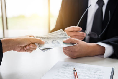 Cropped hand of client giving paper currency to businessman on office desk