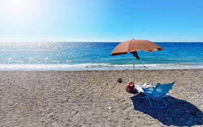 A deckchair under an umbrella facing the blue sea in a stony beach in sicily, italy. summer holidays 