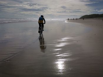 Rear view of man cycling on beach