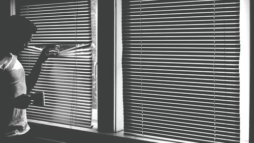 Man peeking through window blinds at home