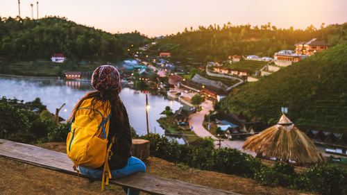 Rear view of woman sitting on seat during sunset