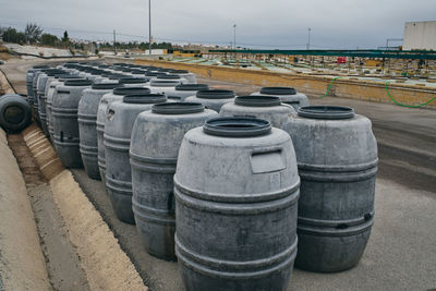 Rows of shabby metal barrels placed in shabby industrial place of factory on cloudy day