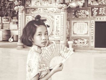 Portrait of girl holding hand fan against building