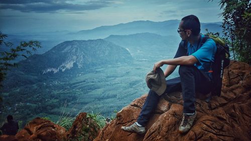 Young man sitting on rock against mountains