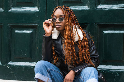 Full length of young woman wearing sunglasses sitting outdoors