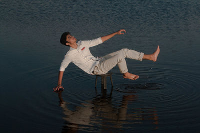 Full length of young man balancing on stool amidst lake