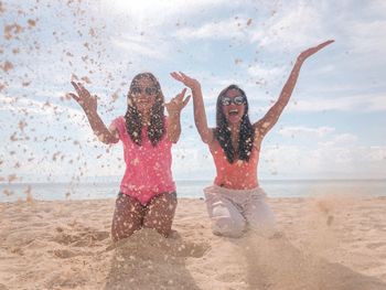 Female friends with arms raised playing in sand at beach