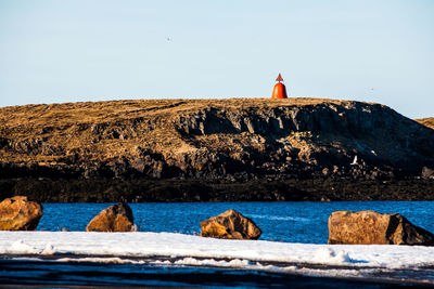 Lighthouse on rock by sea against clear sky