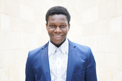 Portrait of smiling young man wearing blue blazer against wall