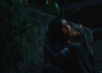 Young woman smoking cigarette while sitting outdoors