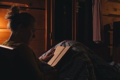 Woman reading book on bed in wooden cottage