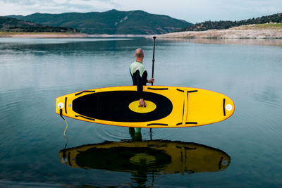 Side view of unrecognizable male surfer in wetsuit standing with yellow sup board and paddle in sea water