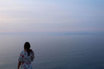 Rear view of woman looking at sea against sky during sunset