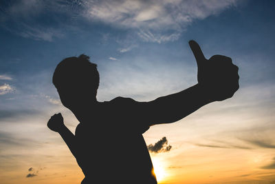 Silhouette man gesturing thumbs up against sky during sunset