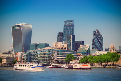 Ferry boats sailing on thames river against modern skyscrapers in city