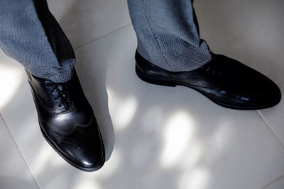 Black leather shoes close up on a man in gray trousers against a background of white tiles