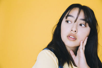 Close-up of girl looking away with hand on chin against yellow background