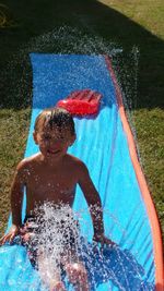 Cute shirtless boy sliding on water slide at backyard