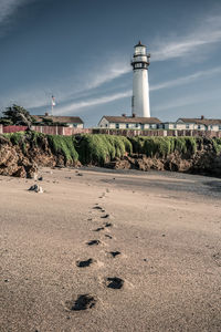 Lighthouse by beach against sky