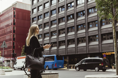 Female entrepreneur with smart phone walking against building