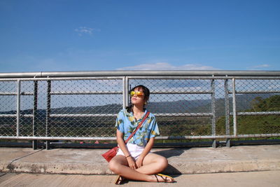 Woman in sunglasses sitting against fence