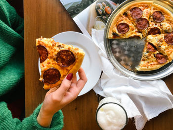 High angle view of hand holding pizza on table